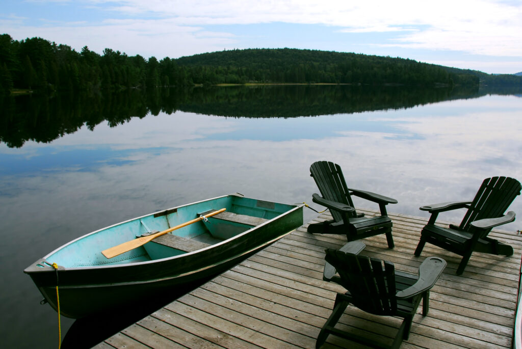 Three wooden adirondack chairs on a boat dock on a beautiful lake in the evening