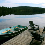 Three wooden adirondack chairs on a boat dock on a beautiful lake in the evening