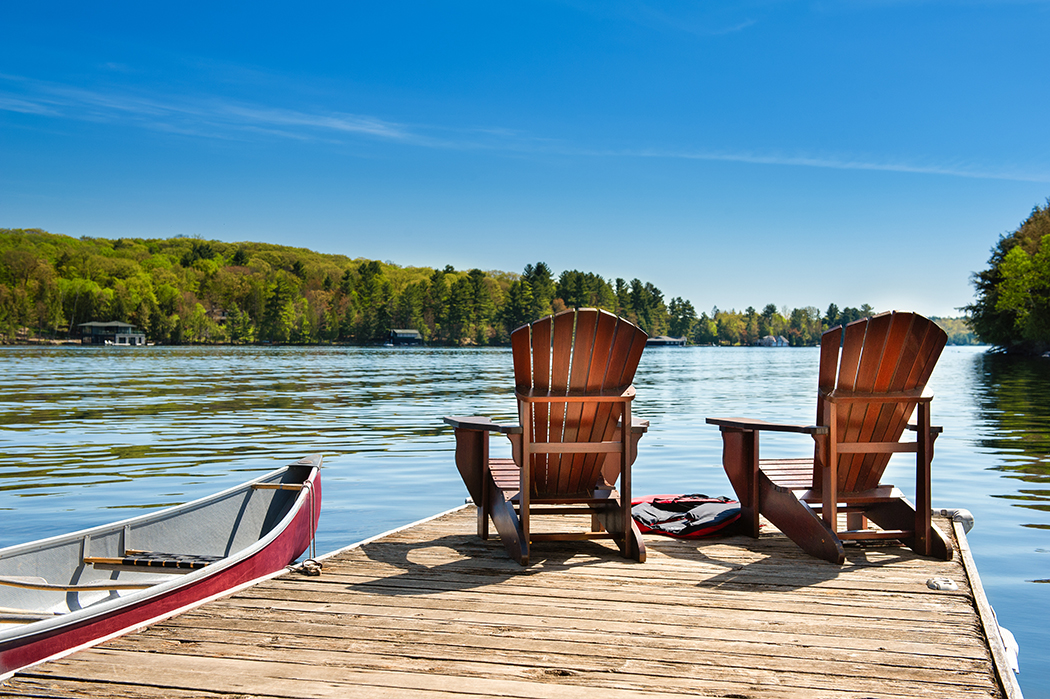 Two Adirondack chairs on a wooden dock on a lake in Muskoka, Ont
